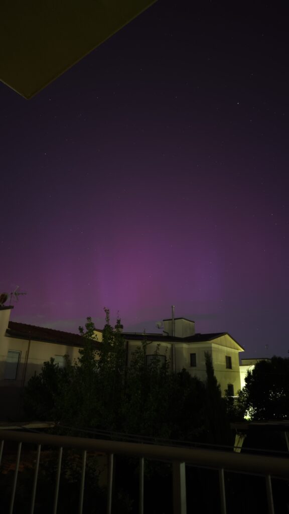 L'immagine è scattata da un balcone, di cui è presente il corrimano in basso, ed è scattata verso il cielo. Nella metà bassa sono presenti delle case e un albero, mentre il resto dell'immagine mostra il cielo di una netta tonalità rosa-viola dovuta all'aurora. Appena sopra i tetti delle case si intravedono delle strisce verticali più chiare, associate al fenomeno aurorale. Sparse per il cielo sono presenti alcune deboli stelle.